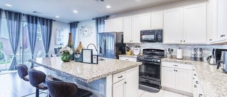 A modern kitchen with white cabinets, a granite countertop, and a large island with bar stools.