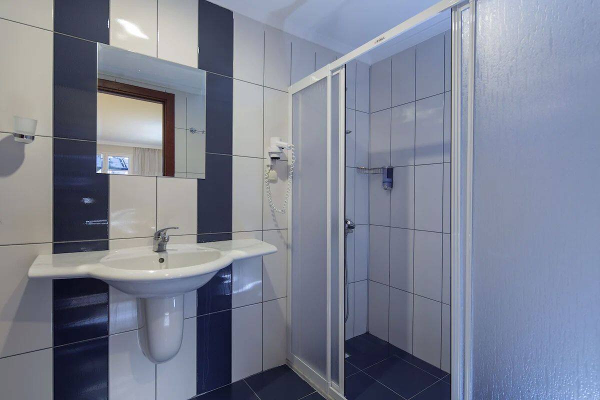 Une salle de bain avec un lavabo blanc, un miroir et un espace douche.