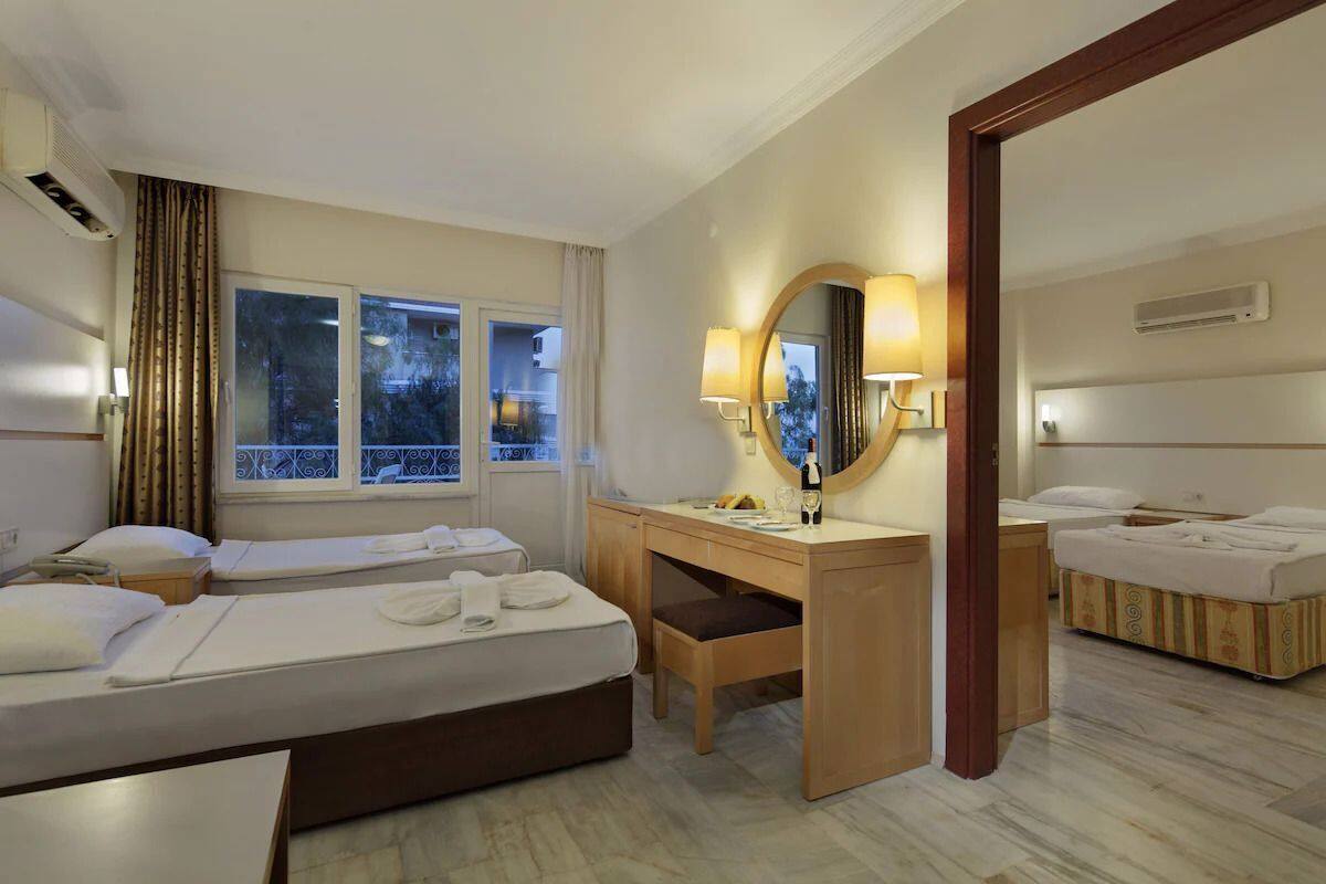 Une chambre d’hôtel avec deux lits, un bureau, une chaise, un miroir et une fenêtre avec des rideaux.