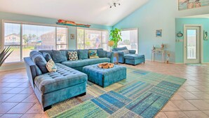 A spacious living room with a sectional sofa, a coffee table, and a large window with blinds.