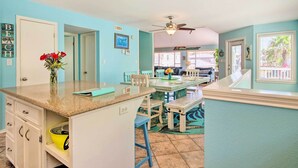 A kitchen with a granite countertop, white cabinets, and a vase with red flowers. There is a dining area with a wooden table and chairs, and a ceiling fan.
