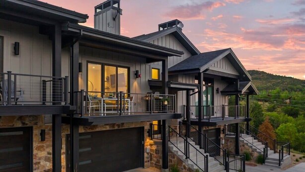 A modern two-story house with a stone facade, large windows, and a balcony with outdoor furniture.