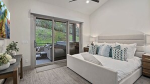 A bedroom with a large bed, a nightstand, a lamp, a ceiling fan, and a sliding glass door leading to an outdoor area with a barbecue.