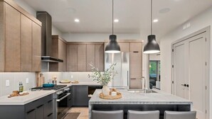 A modern kitchen with dark cabinetry, a central island with bar stools, stainless steel appliances, and pendant lighting.