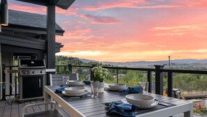 An outdoor dining area with a table set for two, a grill, and a scenic view of the landscape.