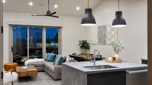 A modern living room with a sofa, coffee table, and a dining area. There is a kitchen with a sink and a dining table.
