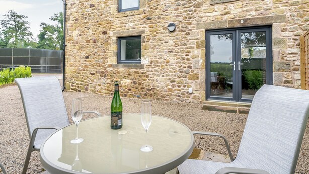 A stone building with a glass table and chairs, a bottle of champagne, and two glasses.