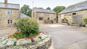 A stone building with a tiled roof, a small garden with colorful flowers, and a paved area in front.