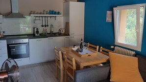 A compact kitchen with white cabinets, a built-in oven, and a dining area with a wooden table and chairs. - 2 Bed Flat - Pets - Pool - Garden - Parking (Borgo Val di Taro)