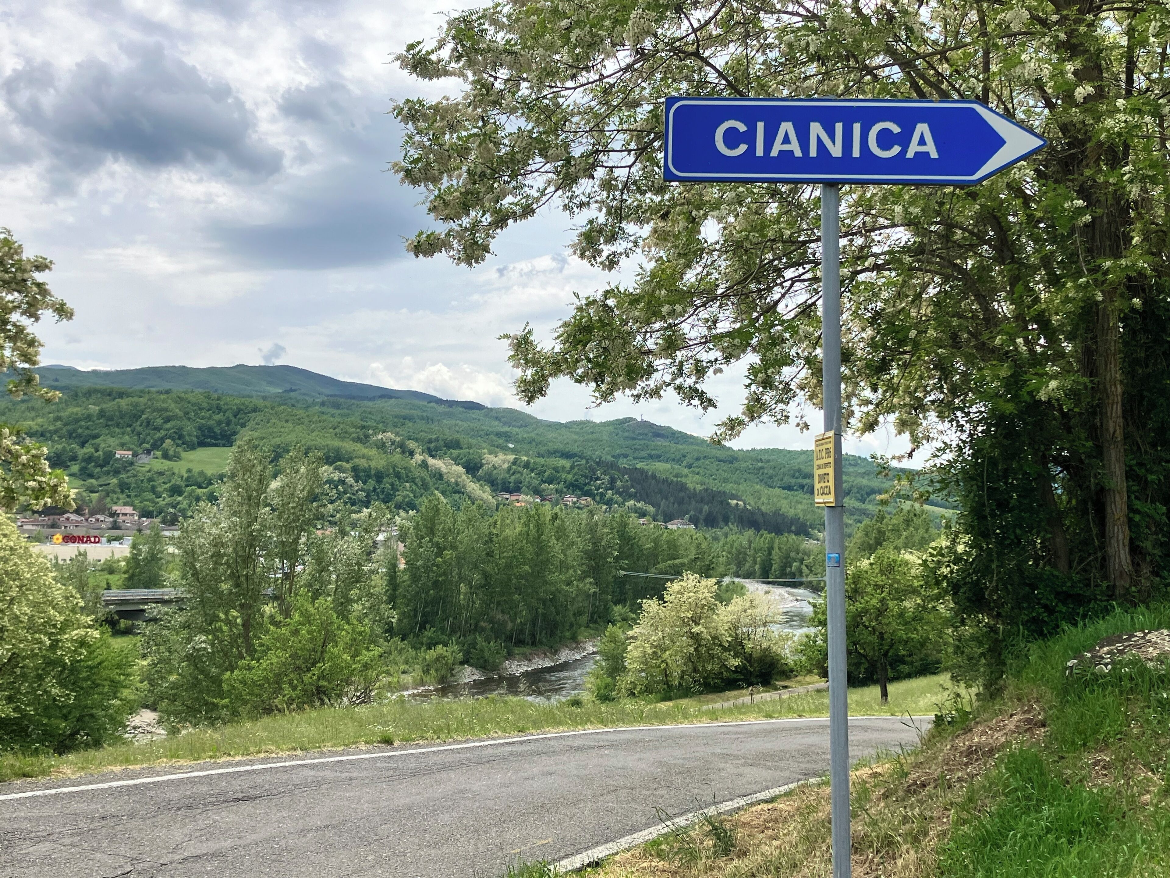 Placa de sinalização para CIANICA, com vista para um rio e montanhas ao fundo.