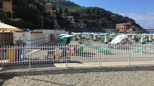 A beach with umbrellas and sun loungers, a white fence, and buildings in the background. - 2 Bed Flat - Pets - Pool - Garden - Parking (Borgo Val di Taro)