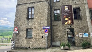 A stone building with multiple windows, a banner advertising a museum, and directional signs. - 2 Bed Flat - Pets - Pool - Garden - Parking (Borgo Val di Taro)