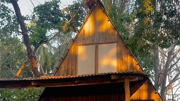 A wooden cabin with a pitched roof, a porch with chairs, and a view of surrounding trees. - Surrounded By Trees In Front Of The Sea (Cóbano)