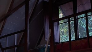 A room with a sloped ceiling, wooden beams, and a window with a view of greenery. - Surrounded By Trees In Front Of The Sea (Cóbano)