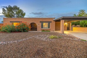 Une maison moderne à deux étages, avec une façade en briques, un patio couvert et une allée gravillonnée.