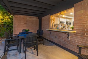 Une terrasse extérieure avec un mur en briques, une table à manger avec des chaises et un luminaire suspendu.