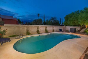 Une piscine à bord incurvé, entourée d’une terrasse en béton. On y trouve des chaises longues et une petite table près de la piscine.