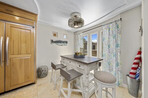 A kitchen with wooden cabinets, a white island with bar stools, a ceiling fan, and a window with curtains. - Best Court South Mission Beach! Steps to Beach & Bay w/ Parking, Bikes & Jacuzzi (San Diego)