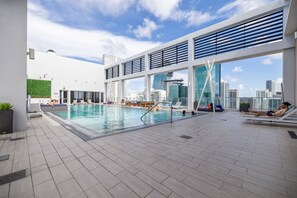 En pool på taket med utsikt över staden, solstolar och en modern arkitektonisk design.