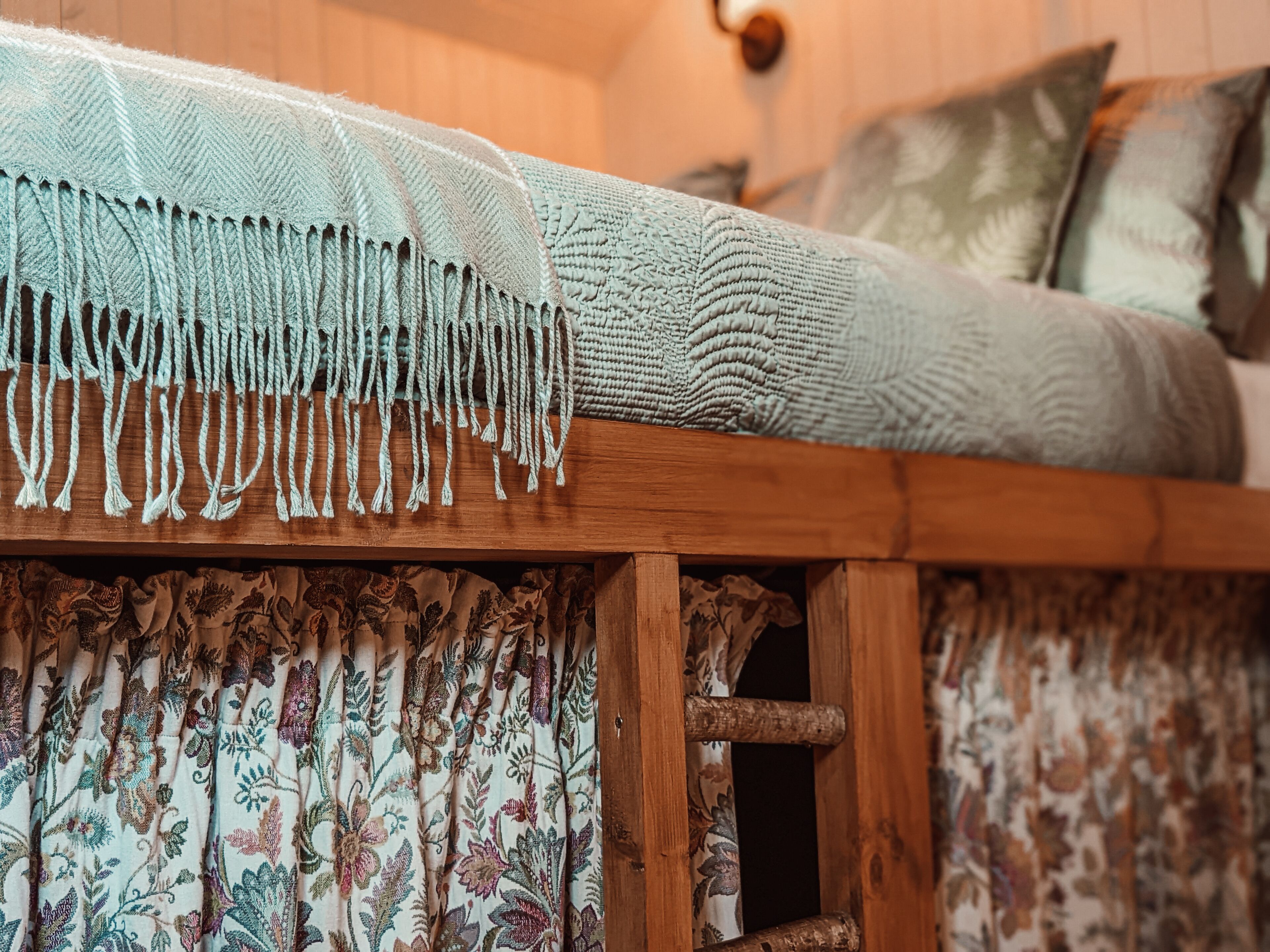 A cozy room with a wooden headboard, a patterned curtain, and a bed with a textured blanket.