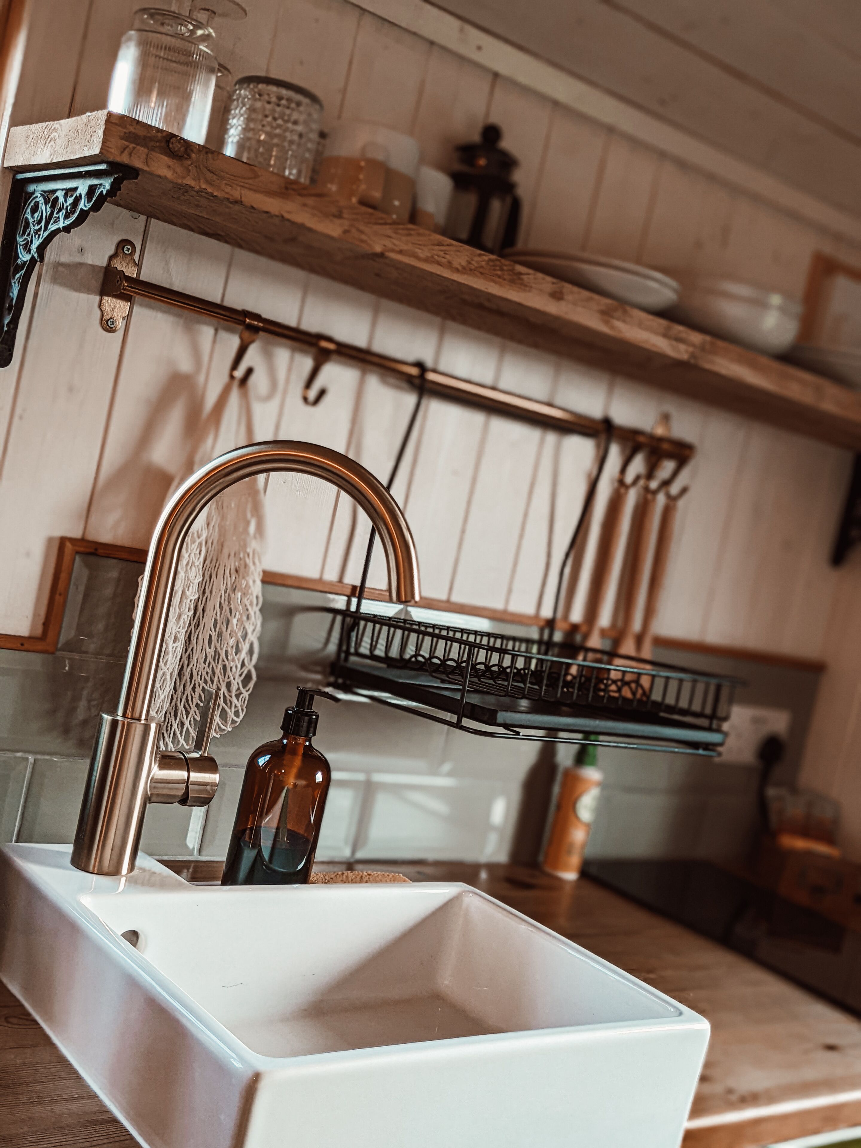 Una cocina con un lavamanos blanco, estantes de madera y utensilios colgando.