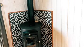 A wood stove with a decorative panel and a basket under it.