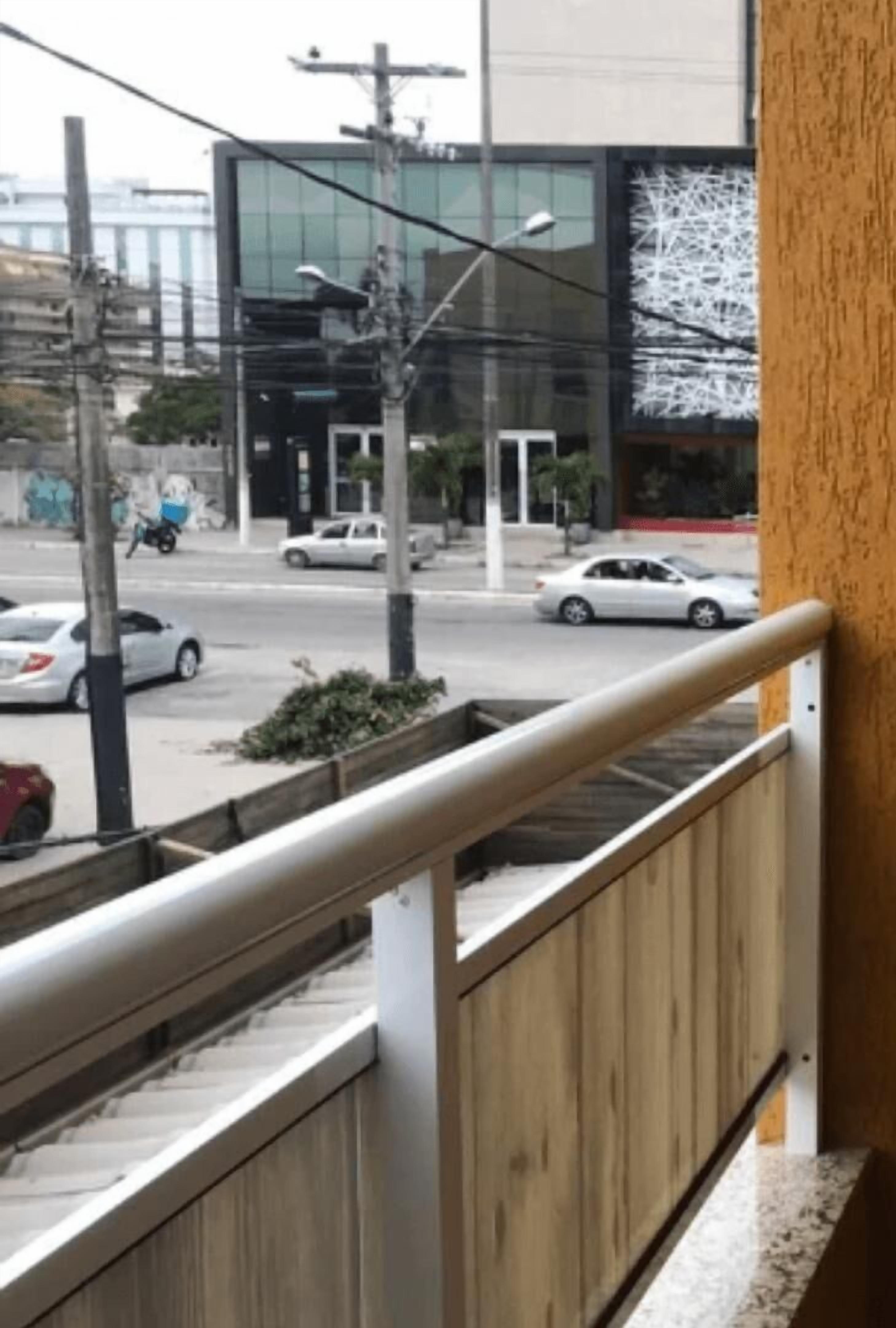 Udsigt fra en balkon over en gade med biler og en bygning med glasfacade.