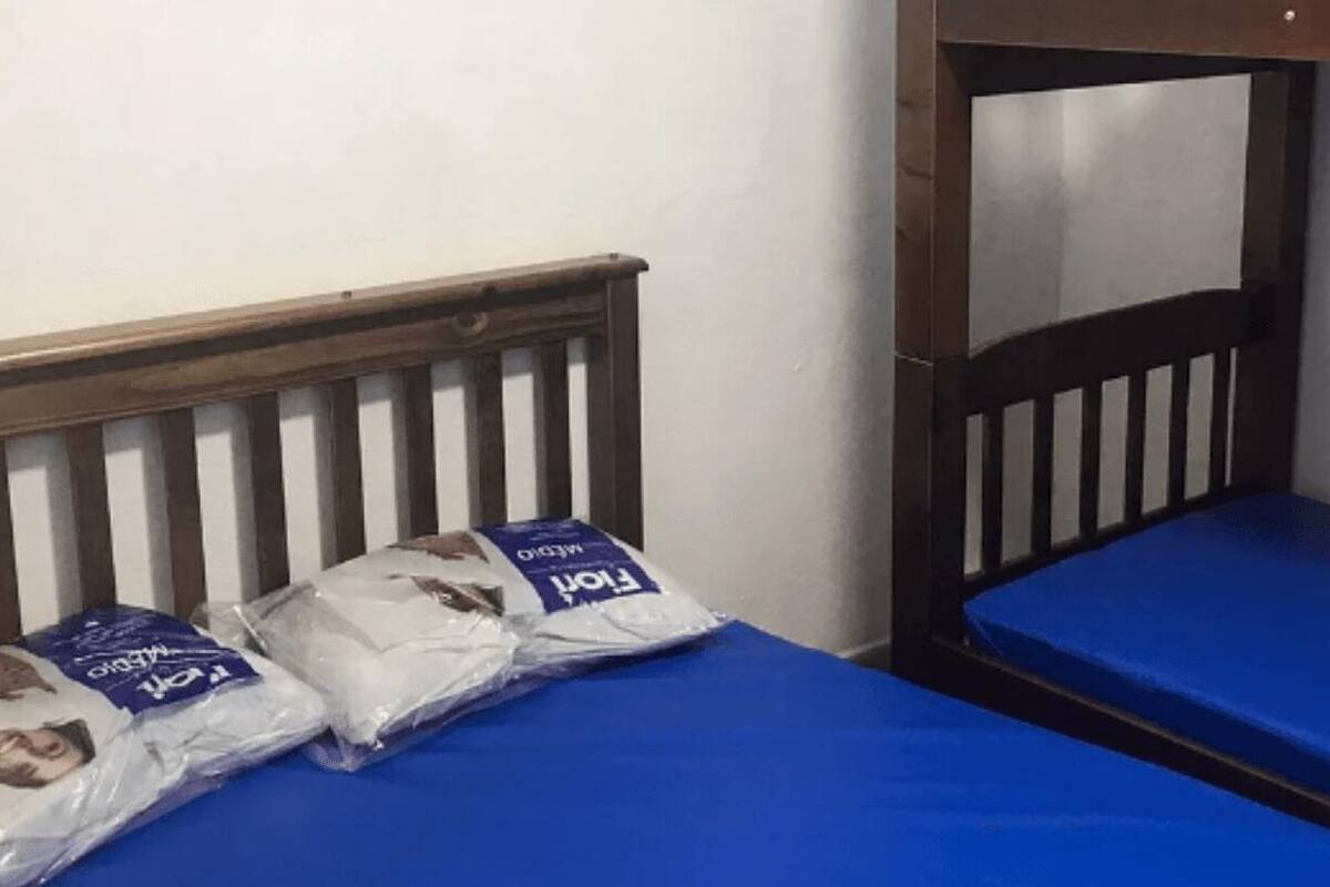 A bunk bed with a blue mattress and a wooden headboard. There are two pillows on the bed, and a window is visible in the background.