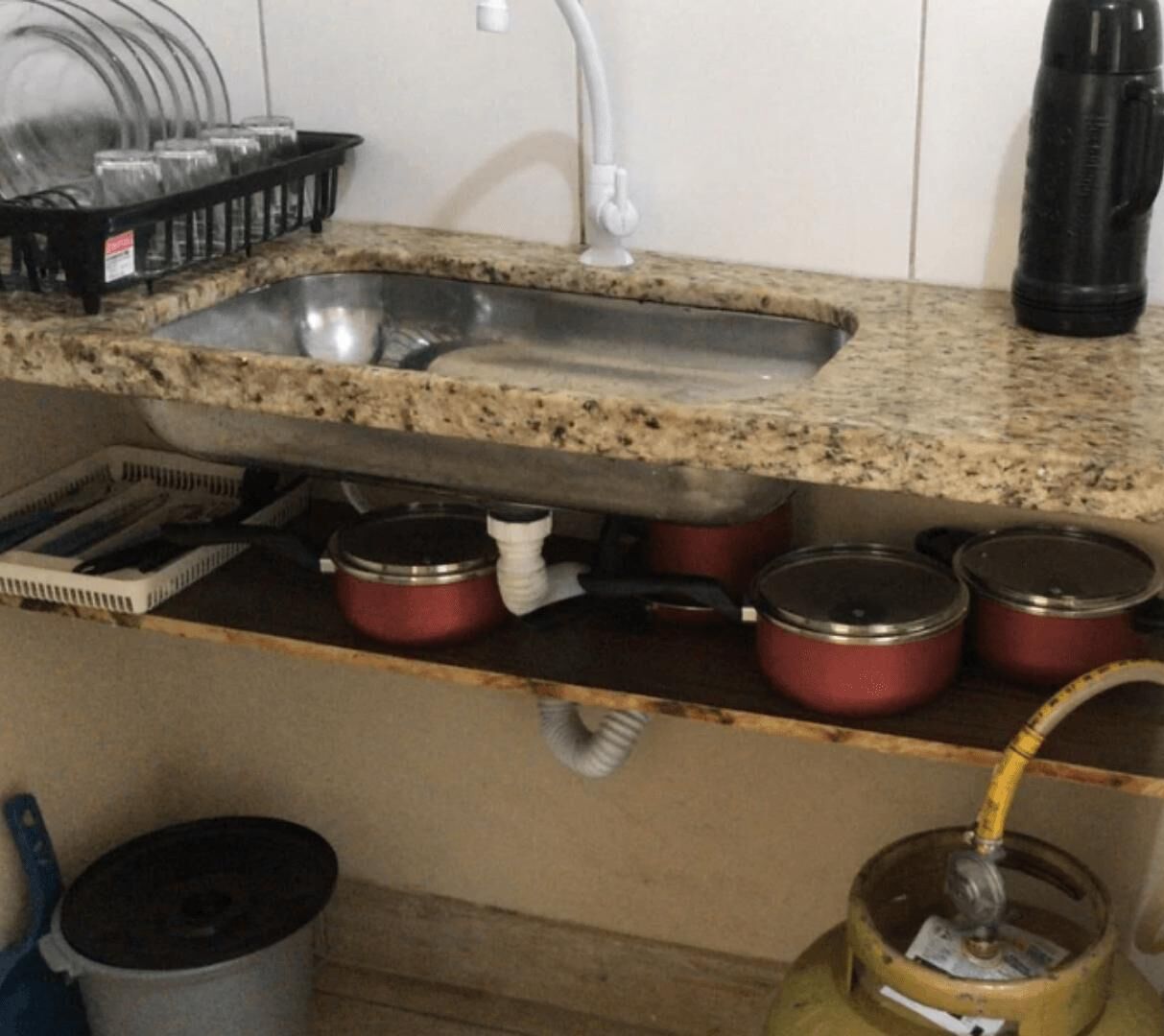 A kitchen with a granite countertop, a stainless steel sink, and several red pots.