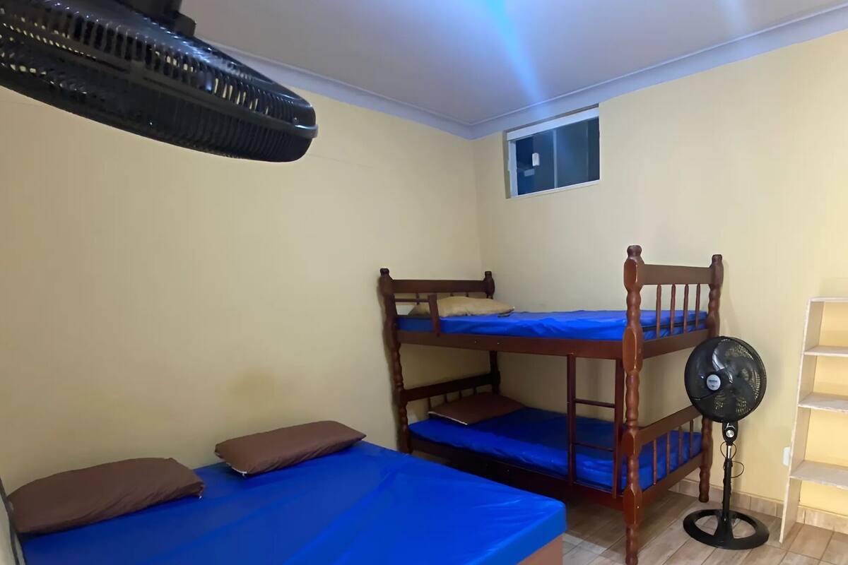 A bunk bed room with a standing fan, a shelf unit, and a window.
