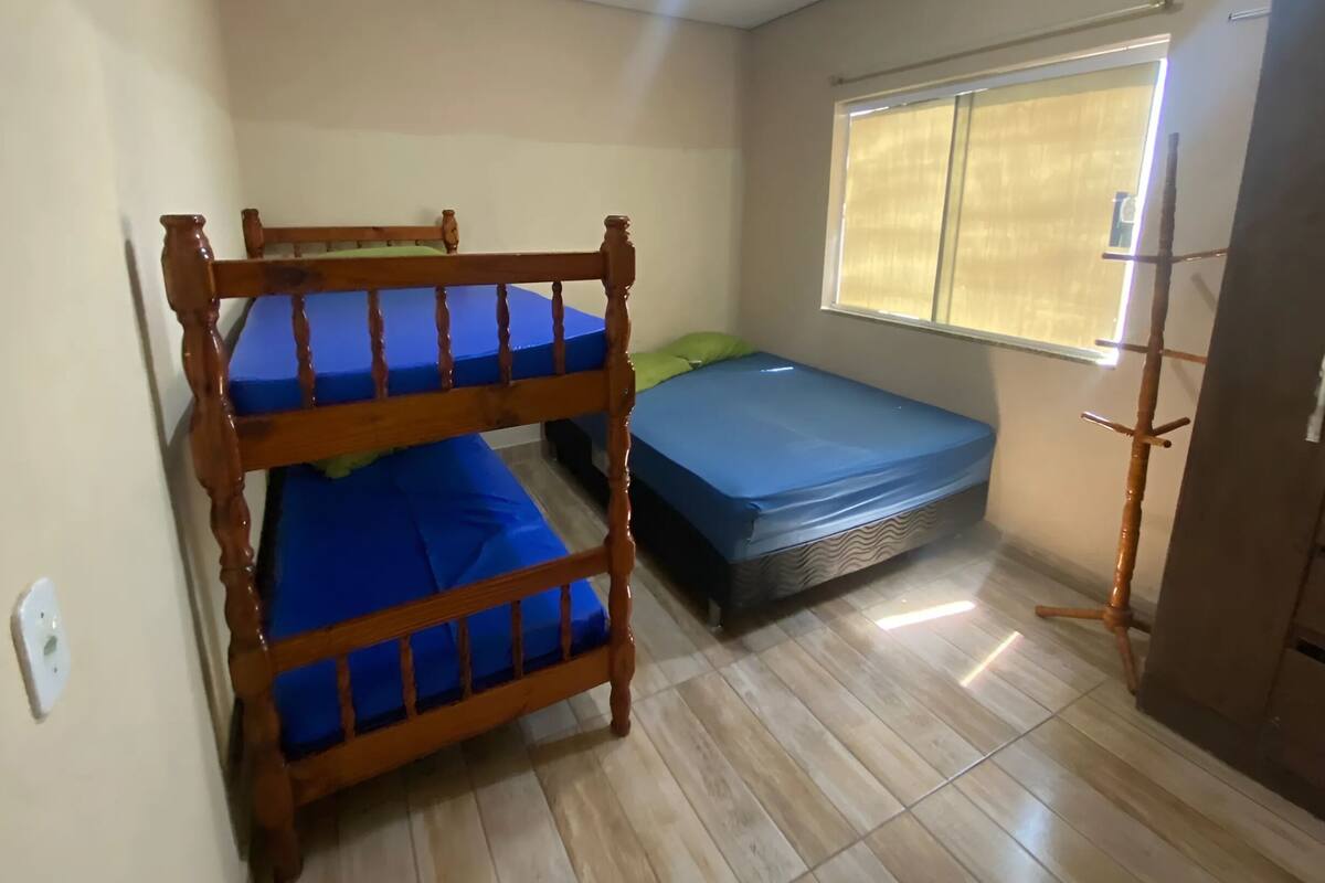 A room with two bunk beds, a single bed, a window with blinds, and a wooden wardrobe.
