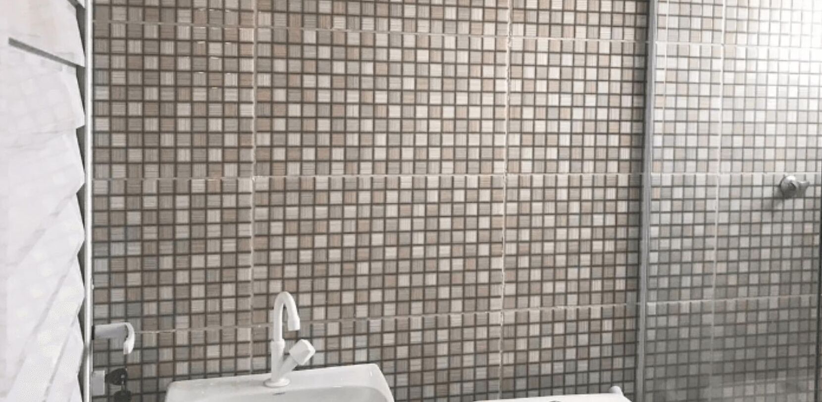 A bathroom with a tiled wall, a sink, and a faucet.