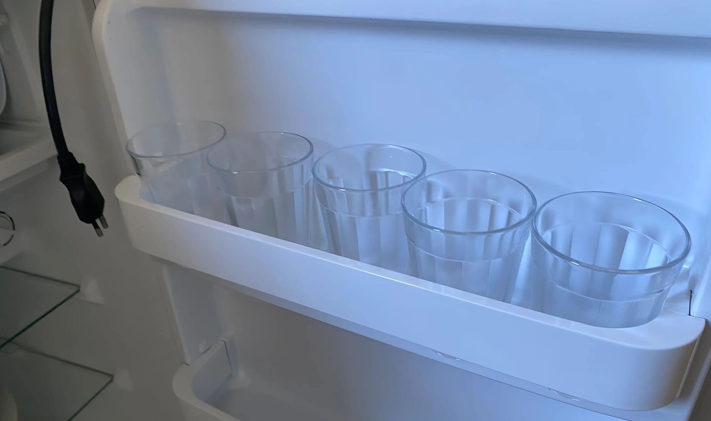 A white refrigerator with a built-in glass storage compartment holding several clear glasses.