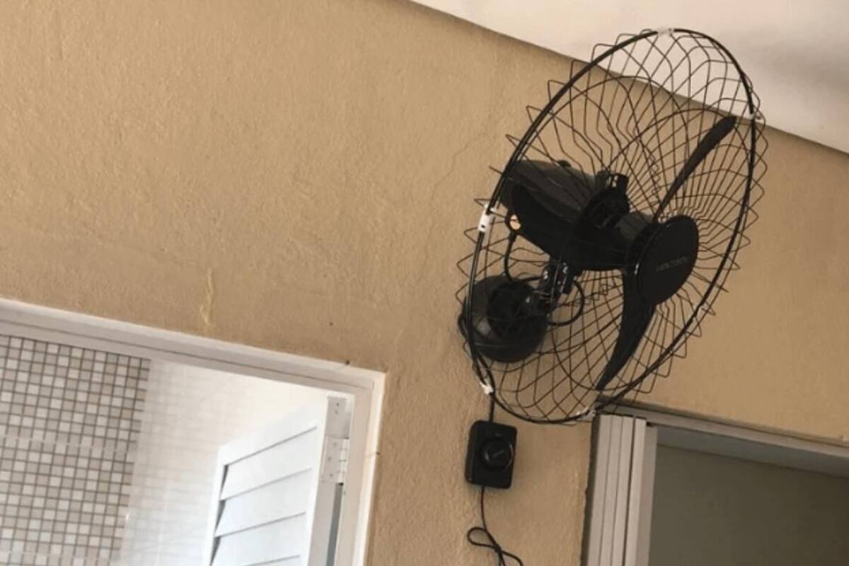 A wall-mounted fan with a control unit attached to a beige wall.