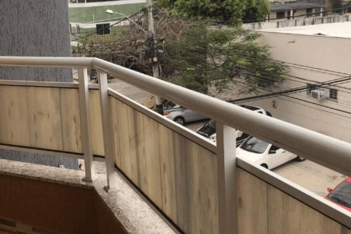 A wooden staircase with a metal handrail leading to a balcony overlooking a street with parked cars.
