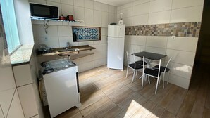 A compact kitchen with a microwave, stove, sink, refrigerator, and a small dining table with chairs. - Jardim Caiçara - Aluguel Economico (Cabo Frio)