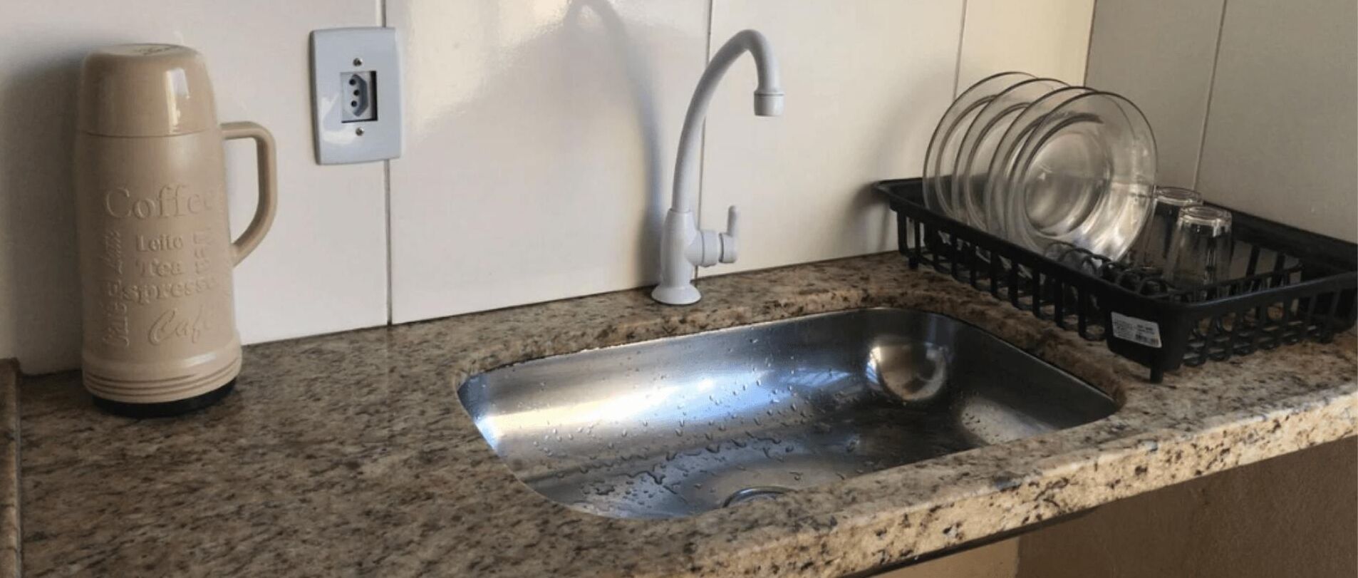 A kitchen with a stainless steel sink, a coffee maker, and a dish rack.