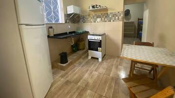 A compact kitchen with a refrigerator, a gas stove, a sink, and a small table.