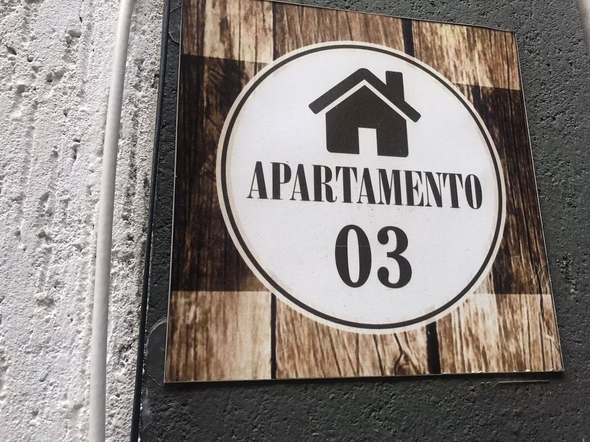Ein Schild mit einem Haus-Symbol und dem Text 'APARTAMENTO 03' auf Holz.