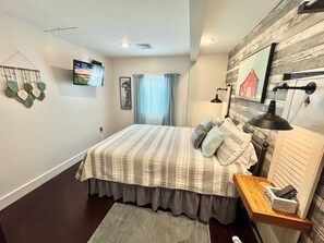Un dormitorio con cama, mesita de noche, lámpara, televisor y una obra de arte colgada en la pared.