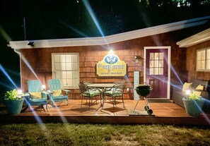 Una casa de madera con un porche, un letrero que dice "The Cozy Corner Guest Houses" y mobiliario exterior.