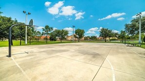 Ein Basketballplatz im Freien mit blauem Himmel und Bäumen im Hintergrund.
