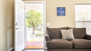 A living room with a brown sofa, a door leading outside, and a wall sign that says "THIS IS MY HAPPY PLACE".