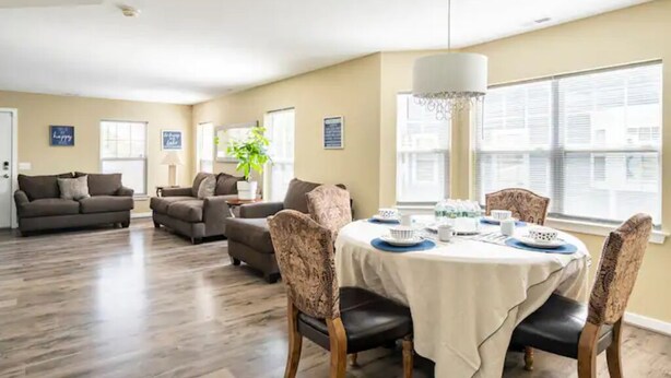 A spacious living room with a dining area, featuring a large window, a chandelier, and a modern interior design.