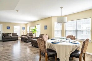 A spacious living room with a dining area, featuring a large window, a chandelier, and a modern interior design.
