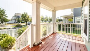 A wooden porch with white railings, a clear view of the street, and a residential neighborhood in the background.