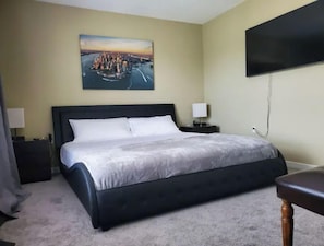A hotel room with a large bed, two bedside tables, a flat-screen TV mounted on the wall, and a painting above the bed.