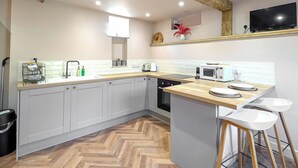 Una cocina moderna con armarios grises, encimera de madera, microondas integrado y una pequeña isla con taburetes.