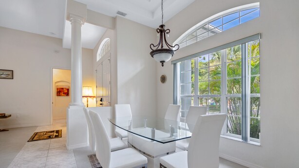 A dining area with a glass table and white chairs, a chandelier, and a large window with a view of palm trees. - Sea Glass Serenity, 3+2, Nokomis Beach, Heated Pool (Nokomis)