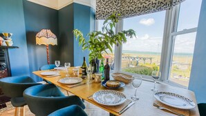 Un coin repas avec une table dressée pour quatre personnes, une plante en pot et une vue sur la mer.